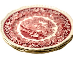 May include: A stack of four red and white decorative plates. Each plate features a detailed red illustration in the center, surrounded by a white border with a scalloped edge. The plates are stacked on top of each other.