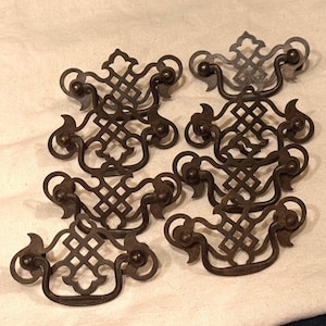 May include: A collection of six dark bronze-toned metal drawer pulls. Each pull features a decorative backplate with a lattice-style cutout pattern and a curved, swinging handle attached by two small ball-shaped mounting points on each side.