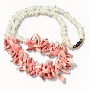 May include: A necklace featuring a white shell bead strand with a coral-like pendant. The pendant is composed of pink, textured pieces, creating a unique and natural aesthetic. The necklace has a brass clasp.