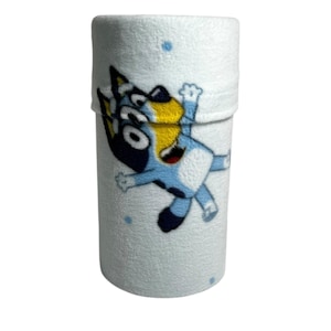 May include: A white, cylindrical plush item featuring a cartoon character in blue, black, and yellow. The character is in a playful pose. Small blue dots are scattered across the white background. The item appears to be a rolled-up blanket or towel.