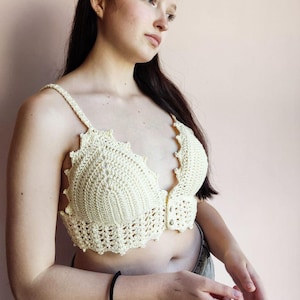 Puede incluir: Top de ganchillo color crema con bordes festoneados y tirantes ajustables. El top hecho a mano presenta un cierre de botón en la parte delantera. Una pieza única de arte portátil.