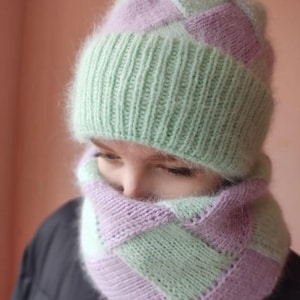 May include: A knitted hat and scarf set in a checkerboard pattern. The hat and scarf are in shades of light green and lilac. The hat has a ribbed brim. The scarf is wrapped around the neck.