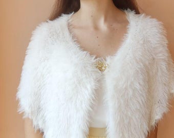 May include: White faux fur shawl with a scalloped edge. The shawl is draped over a person's shoulders and is fastened with a small, decorative brooch.