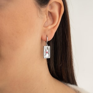 May include: Silver earring with a tarot card charm featuring The Lovers card with a red heart and the text "The Lovers".