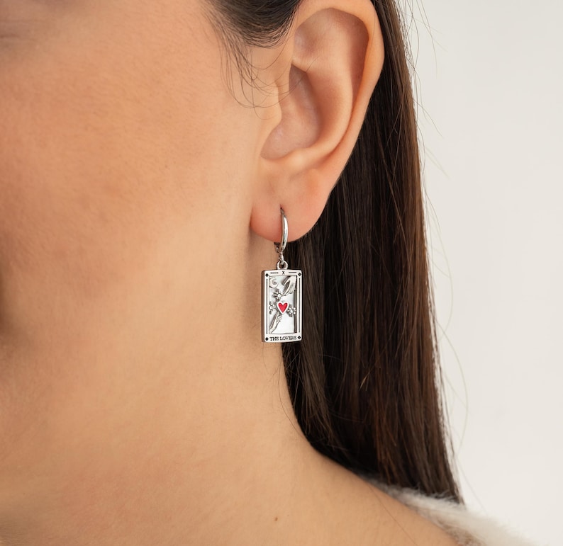 May include: Silver earring with a tarot card charm featuring The Lovers card with a red heart and the text "The Lovers".