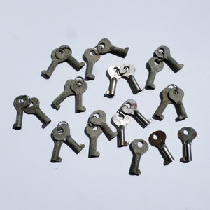 May include: A collection of vintage keys, all made of metal and painted in a silver color. The keys are arranged in a random pattern on a white surface.