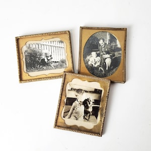 May include: Three gold-toned picture frames with black and white photos of a child and a dog. The frames have ornate edges.