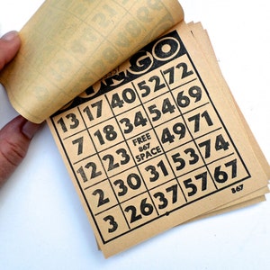 Puede incluir: Un juego de tarjetas de bingo de papel marr&oacute;n con n&uacute;meros negros impresos en ellas. Los n&uacute;meros en las tarjetas son 13, 17, 40, 52, 72, 7, 18, 34, 54, 69, 12, 23, 49, 71, 2, 30, 31, 53, 74, 3, 26, 37, 57, 67. La palabra "Bingo" est&aacute; impresa en la parte superior de las tarjetas.