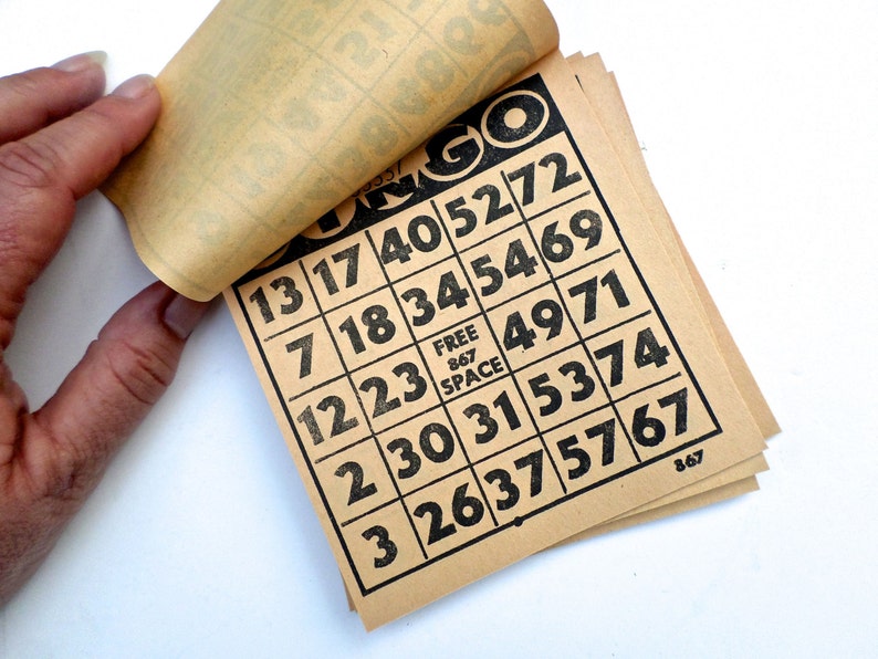 Puede incluir: Un juego de tarjetas de bingo de papel marr&oacute;n con n&uacute;meros negros impresos en ellas. Los n&uacute;meros en las tarjetas son 13, 17, 40, 52, 72, 7, 18, 34, 54, 69, 12, 23, 49, 71, 2, 30, 31, 53, 74, 3, 26, 37, 57, 67. La palabra "Bingo" est&aacute; impresa en la parte superior de las tarjetas.