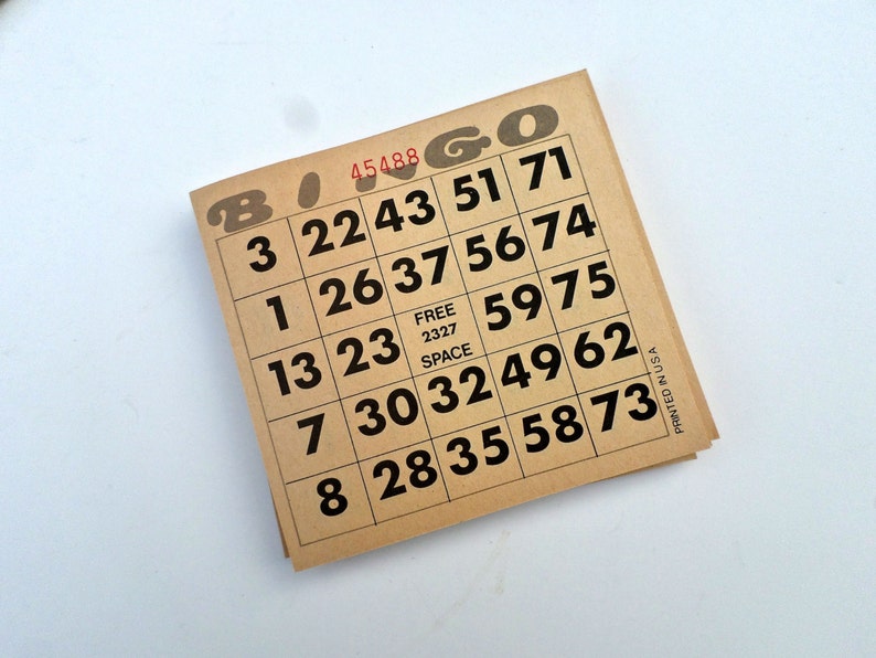 Puede incluir: Un cart&oacute;n de bingo marr&oacute;n con n&uacute;meros negros y la palabra "Bingo" impresa en letras rojas. El cart&oacute;n tiene un espacio libre en el centro y los n&uacute;meros 3, 22, 43, 51, 71, 1, 26, 37, 56, 74, 13, 23, 59, 75, 7, 30, 32, 49, 62, 8, 28, 35, 58, 73.