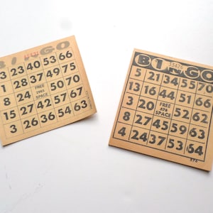 Puede incluir: Dos tarjetas de bingo de papel marr&oacute;n con n&uacute;meros negros. La tarjeta superior tiene los n&uacute;meros 13, 23, 40, 53, 66, 1, 28, 37, 49, 75, 8, 24, 50, 70, 15, 27, 42, 57, 67, 3, 26, 36, 54, 63. La tarjeta inferior tiene los n&uacute;meros 5, 21, 34, 55, 70, 13, 16, 44, 51, 66, 3, 20, 52, 62, 8, 27, 45, 59, 63, 4, 24, 37, 53, 64. Ambas tarjetas tienen la palabra "Bingo" impresa en ellas.