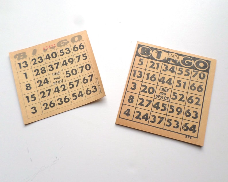 Puede incluir: Dos tarjetas de bingo de papel marr&oacute;n con n&uacute;meros negros. La tarjeta superior tiene los n&uacute;meros 13, 23, 40, 53, 66, 1, 28, 37, 49, 75, 8, 24, 50, 70, 15, 27, 42, 57, 67, 3, 26, 36, 54, 63. La tarjeta inferior tiene los n&uacute;meros 5, 21, 34, 55, 70, 13, 16, 44, 51, 66, 3, 20, 52, 62, 8, 27, 45, 59, 63, 4, 24, 37, 53, 64. Ambas tarjetas tienen la palabra "Bingo" impresa en ellas.