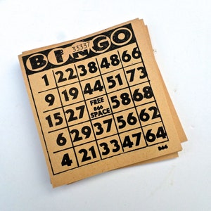 Puede incluir: Un cart&oacute;n de bingo marr&oacute;n con n&uacute;meros negros y la palabra "BINGO" impresa en negro en la parte superior. Los n&uacute;meros en el cart&oacute;n son 1, 22, 38, 48, 66, 9, 19, 44, 51, 73, 15, 27, 58, 68, 6, 29, 37, 56, 62, 4, 21, 33, 47, 64. El cart&oacute;n tambi&eacute;n tiene un cuadrado "CASILLA LIBRE" en el centro.