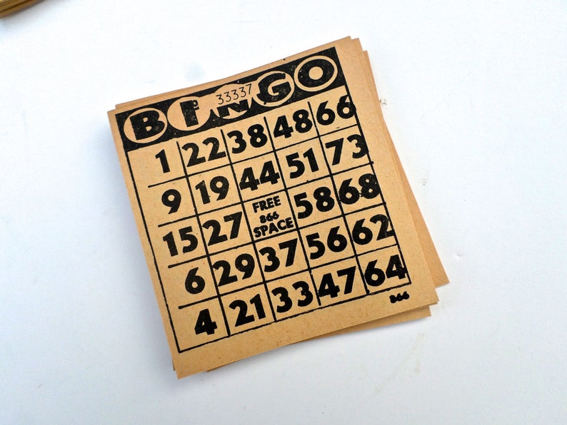 Puede incluir: Un cart&oacute;n de bingo marr&oacute;n con n&uacute;meros negros y la palabra "BINGO" impresa en negro en la parte superior. Los n&uacute;meros en el cart&oacute;n son 1, 22, 38, 48, 66, 9, 19, 44, 51, 73, 15, 27, 58, 68, 6, 29, 37, 56, 62, 4, 21, 33, 47, 64. El cart&oacute;n tambi&eacute;n tiene un cuadrado "CASILLA LIBRE" en el centro.
