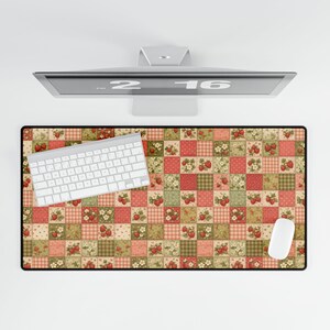 May include: A rectangular desk mat with a patchwork design featuring strawberries, flowers, and plaid patterns in red, green, and beige. A white keyboard and mouse are on the mat, with a computer monitor above.
