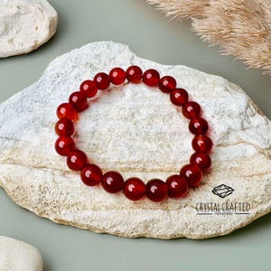 Carnelian gemstone bracelet resting on a natural stone surface with dried plants, showcasing its deep red hue and polished 8mm beads.