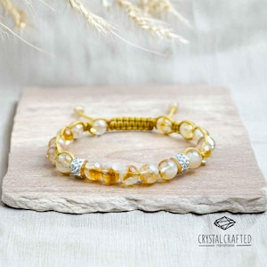 Puede incluir: Una pulsera de citrino hecha a mano con un cordón de macramé y cierre ajustable. La pulsera presenta cuentas de citrino facetadas y espaciadores de pedrería plateados. La pulsera se muestra sobre una superficie de piedra de color neutro. La marca "CRYSTAL CRAFTED Handmade" es visible.