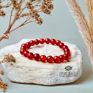 Handcrafted Carnelian stretch bracelet on a soft beige backdrop with earthy dried flowers, exuding warmth and power.