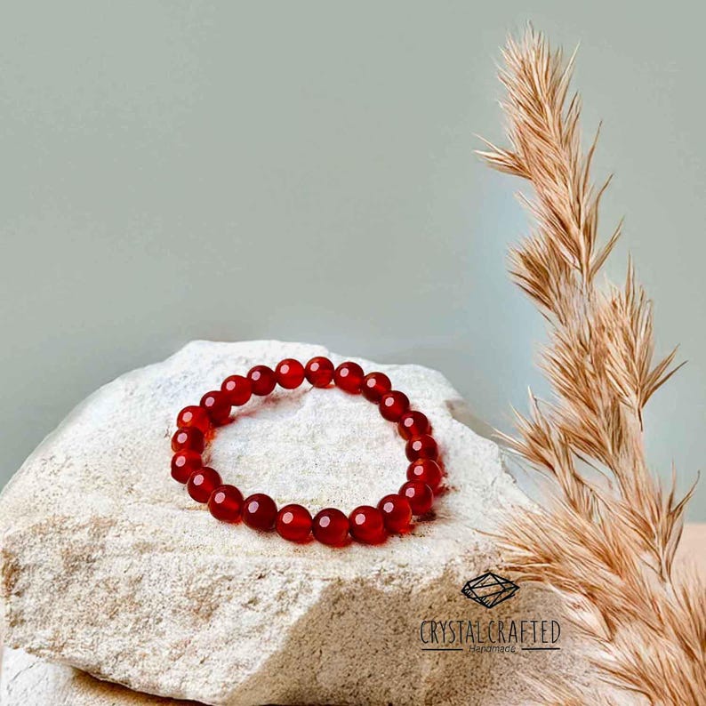 Handmade Carnelian bracelet displayed on a rustic rock with dried grass, highlighting its vibrant color and grounding energy.