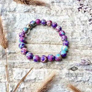 A beautifully crafted stretch bracelet, made of 8mm Sea Sediment Jasper beads, resting on textured stone with soft natural lighting.