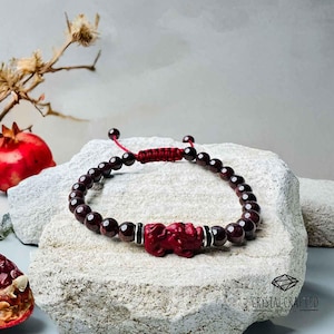 May include: A red gemstone bracelet with a red carved animal charm. The bracelet is made with small round beads and a red string closure.
