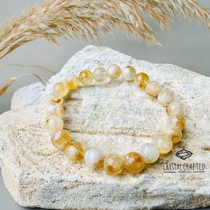 Citrine bracelet resting on natural rock with soft, dried wheat accents, representing its connection to abundance and positive energy.