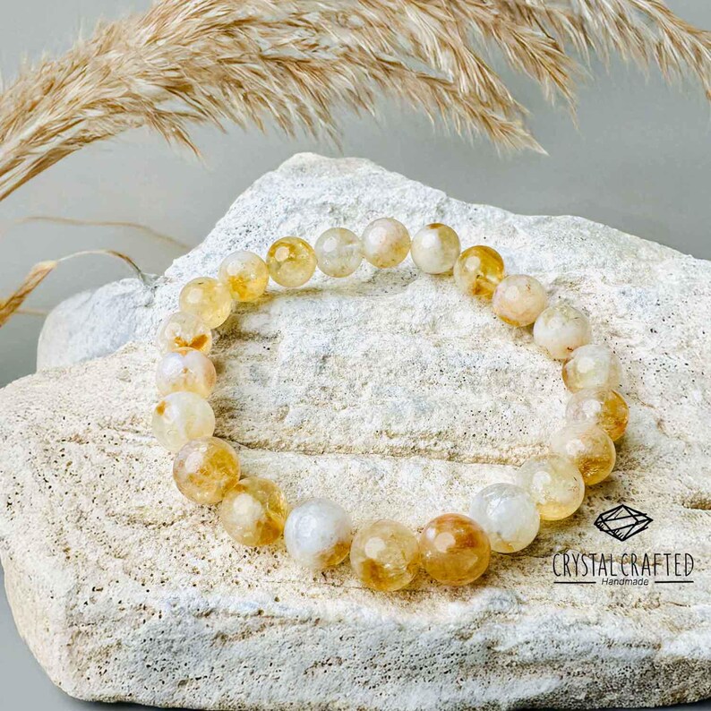 Citrine bracelet resting on natural rock with soft, dried wheat accents, representing its connection to abundance and positive energy.
