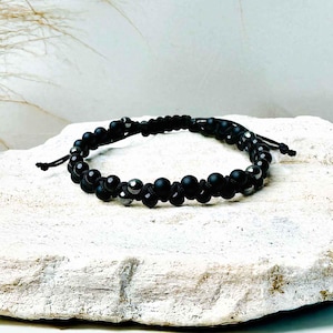 Pode incluir: Pulseira de contas pretas com um cordão de nó. A pulseira tem contas pretas e prateadas.