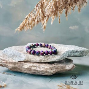 A minimalist, nature-inspired photo featuring the handmade crystal bracelet lying on a textured stone surface, with golden wheat accents.