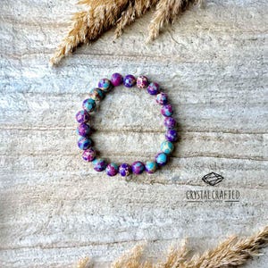 Elegant stretch bracelet made of 8mm Sea Sediment Jasper stones, placed on a neutral rock background with dried botanical accents.