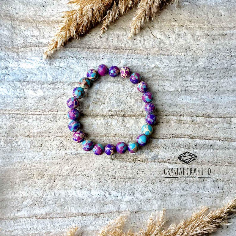 Elegant stretch bracelet made of 8mm Sea Sediment Jasper stones, placed on a neutral rock background with dried botanical accents.