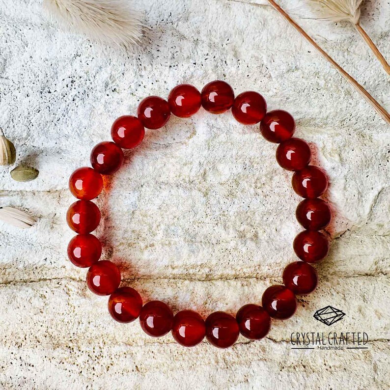Elegant Carnelian bracelet flat-laid on a textured stone surface, surrounded by natural elements, ideal for chakra healing and confidence boosting.