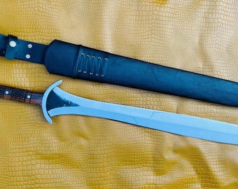 May include: A silver sword with a brown wooden handle and a black leather scabbard. The sword has a curved blade and a pointed tip.