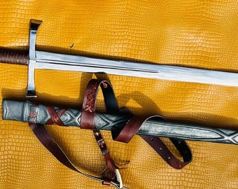 May include: A silver sword with a brown leather handle and a matching scabbard with a brown leather strap. The sword and scabbard are lying on a yellow textured surface.