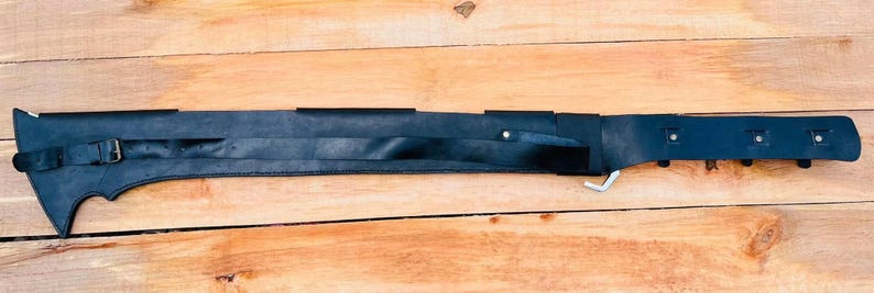 May include: A black leather scabbard with a strap and buckle. The scabbard has a pointed tip and a decorative design on the front.