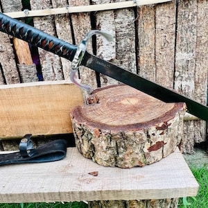 May include: A black sword with a leather handle and a silver guard. The sword is resting on a wooden log.