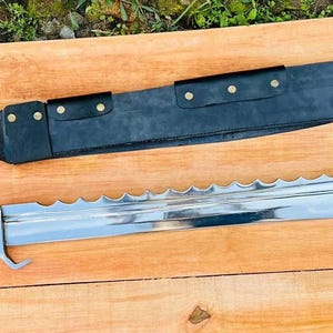 May include: A large, silver, serrated sword with a black leather scabbard. The sword has a wooden handle with a brass pommel. The scabbard has a decorative design with brass accents.