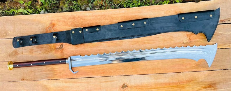 May include: A large, silver, serrated sword with a black leather scabbard. The sword has a wooden handle with a brass pommel. The scabbard has a decorative design with brass accents.