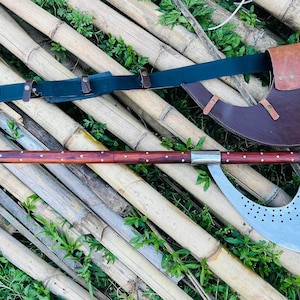 May include: A large, curved axe with a wooden handle and a leather scabbard. The axe blade is silver with a pattern of small holes. The scabbard is brown leather with a decorative strap.