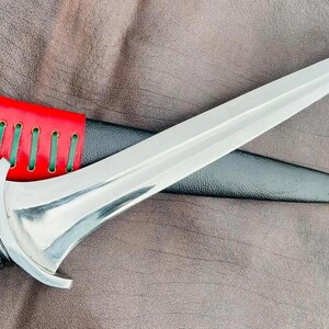 May include: A silver dagger with a red and black leather sheath. The dagger has a decorative handle and a sharp point.