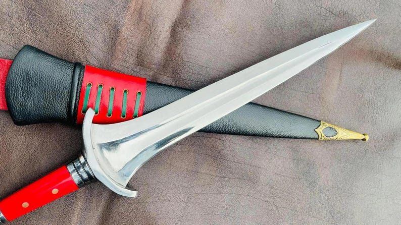 May include: A silver dagger with a red and black leather sheath. The dagger has a decorative handle and a sharp point.