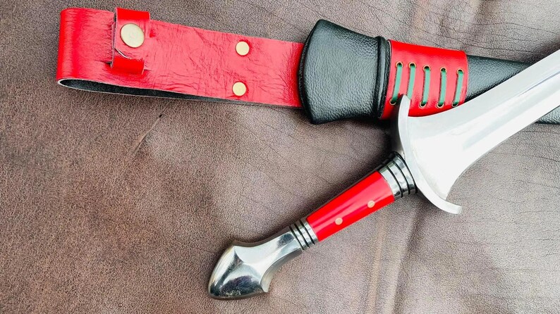 May include: A silver dagger with a red and black handle and a leather sheath with gold accents.