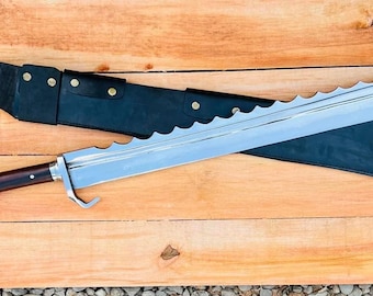 Puede incluir: Una espada grande, plateada, dentada con un mango de madera marrón oscuro y una vaina de cuero negro. La espada está sobre una superficie de madera.