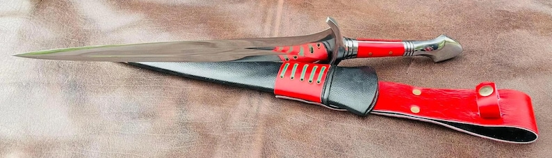 May include: A red and silver dagger with a black leather sheath. The dagger has a decorative handle and a sharp blade.
