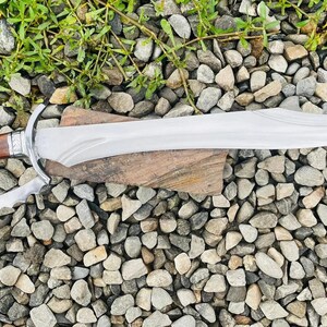 以下が含まれることがあります： 湾曲した刃と鋸歯状の刃を持つ銀と茶色の短剣。短剣は小さな灰色の石のベッドの上に置かれています