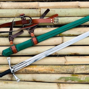 May include: A green and brown leather scabbard with a silver sword with a black handle. The sword and scabbard are lying on a surface of bamboo sticks.