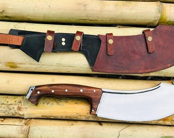 May include: A curved, stainless steel knife with a wooden handle and a leather sheath. The knife has a curved blade and a pointed tip. The sheath is brown leather with stitching around the edges.