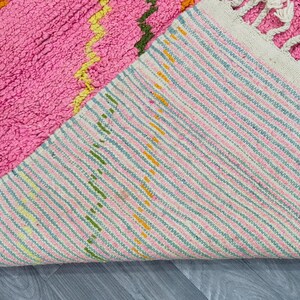 May include: A pink and white woven rug with a striped pattern. The rug has a fringe on one side and is folded in half.