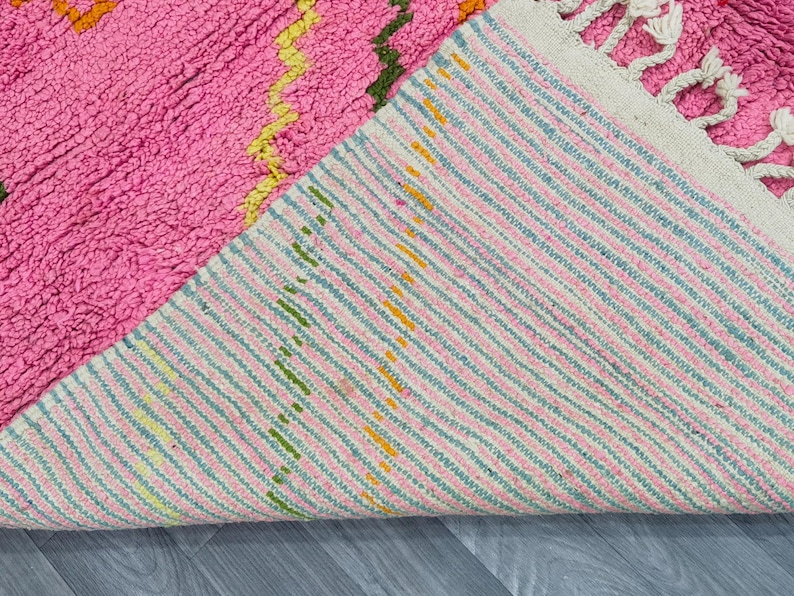 May include: A pink and white woven rug with a striped pattern. The rug has a fringe on one side and is folded in half.