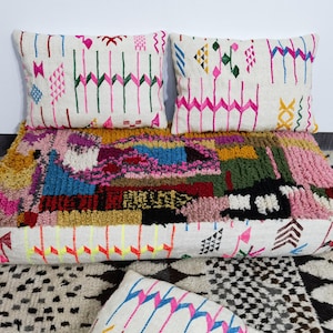 Può includere: Un cuscino da pavimento colorato in stile patchwork con due cuscini abbinati. Il cuscino e i cuscini presentano disegni geometrici in rosa, verde, giallo e blu su sfondo bianco. Il cuscino è largo circa 76 cm.